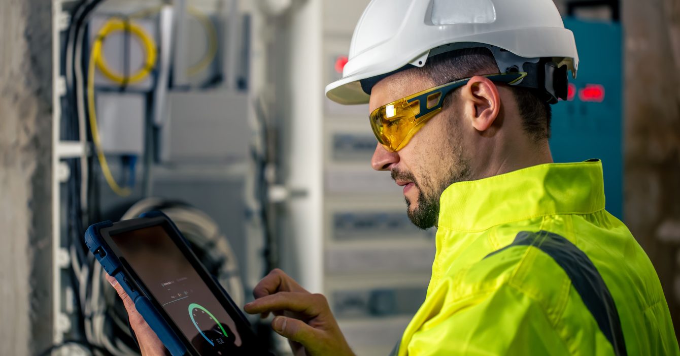 man-electrical-technician-working-switchboard-with-fuses-uses-tablet (1)