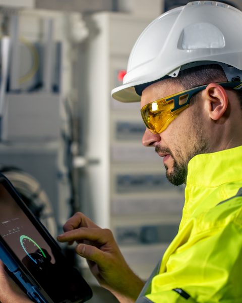 man-electrical-technician-working-switchboard-with-fuses-uses-tablet (1)